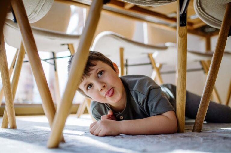 child with his tongue out under a table and chairs